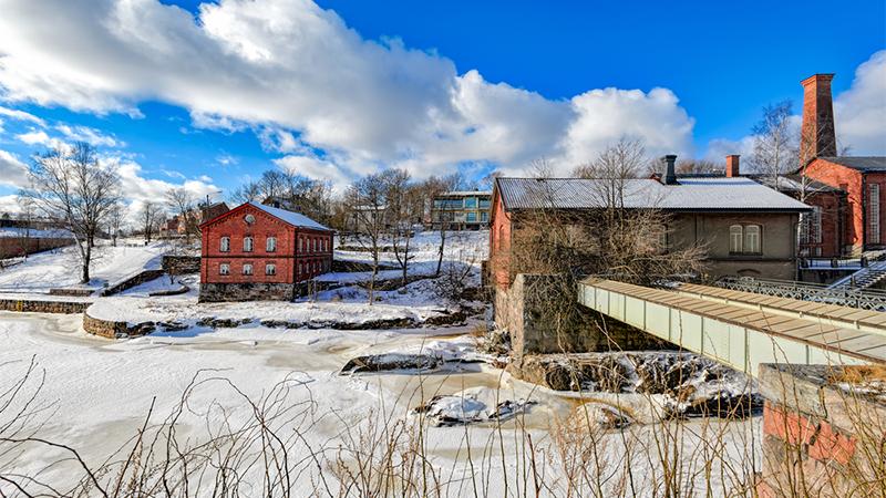 Red brick buildings of former baize factory converted to the museum of Technology in snow covered Verkatehdas Park in mouth of frozen Vantaanjoki river in Helsinki, Finland at sunny winter day